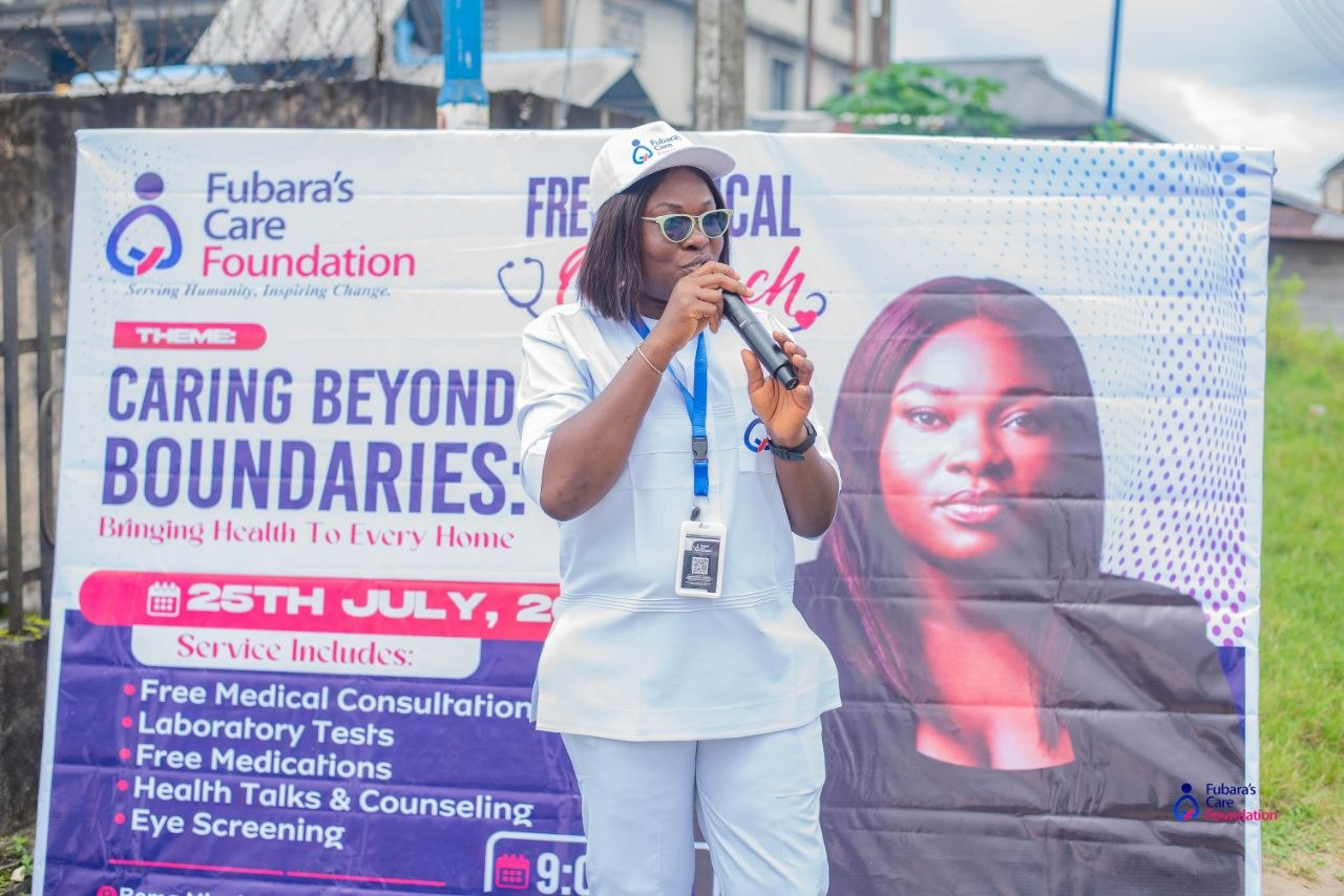 Founder Braide Faustina Fubara addressing the community beside the 'Caring Beyond Boundaries: Bringing Health To Every Home' outreach banner